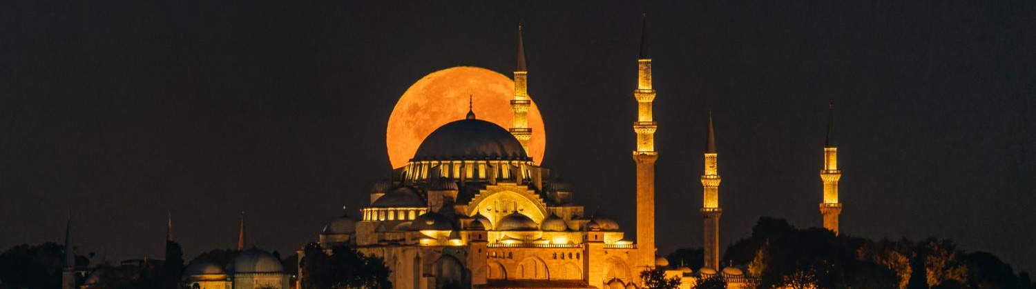 Exterior view of the suleymaniye mosque at midnight with its lights on and moon on the background of the mosque